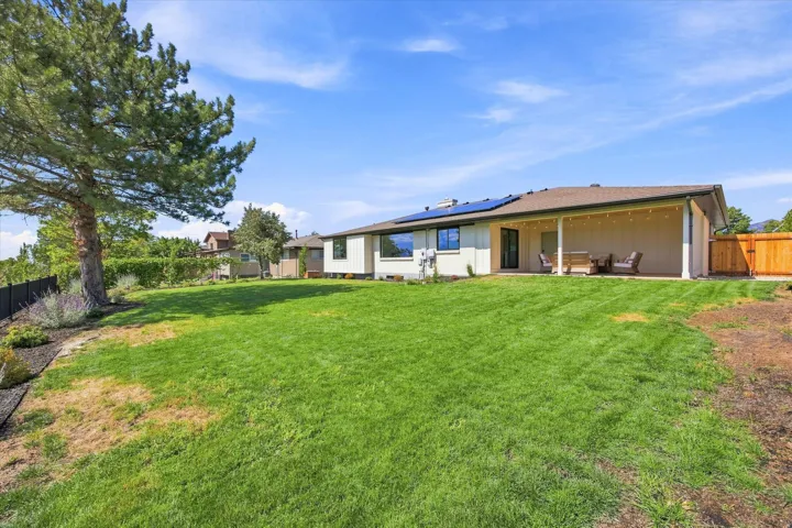 Expansive grassy backyard featuring a large patio cover, solar panels, and a wood privacy fence
