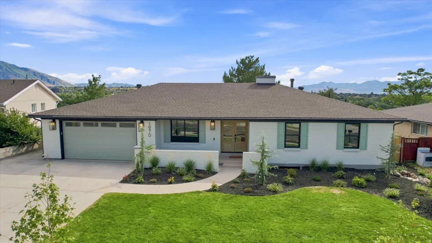 White brick exterior with a brown shingle roof, attached garage, and a landscaped front yard with a concrete walkway