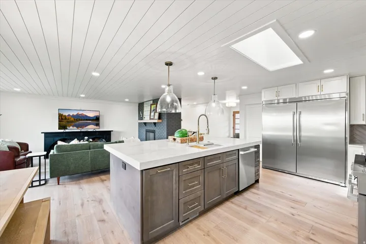 Kitchen island with light-toned countertop, stainless steel refrigerator, wood-finish flooring, and shiplap ceiling