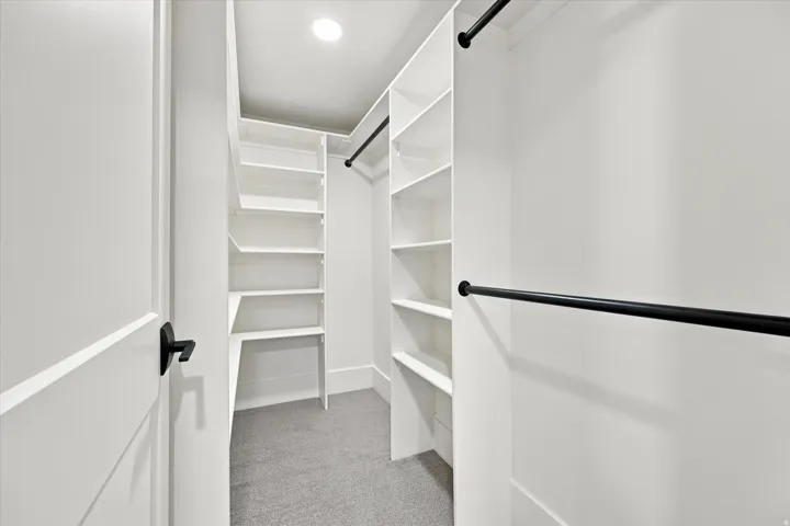 Walk-in closet with built-in shelving, black hanging rods, and recessed lighting