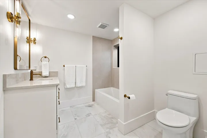 White vanity with a stone countertop, an undermount sink, and a wall-mounted mirror