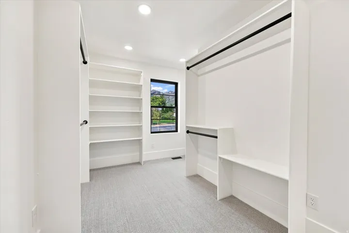 Built-in shelving, integrated hanging rods, recessed lighting, and a window with black trim