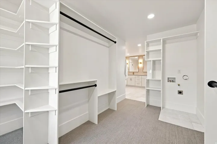 Built-in shelving, black hanging rods, recessed lighting, and laundry hookups with a tiled floor section
