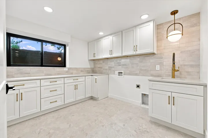 White cabinetry, light-toned countertop, tile backsplash, undermount sink with brass faucet, and recessed lighting