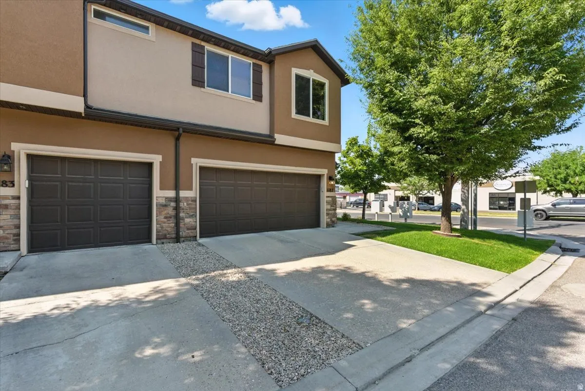 Exterior featuring stucco siding, stone accents, two paneled garage doors, and concrete driveway with gravel detailing