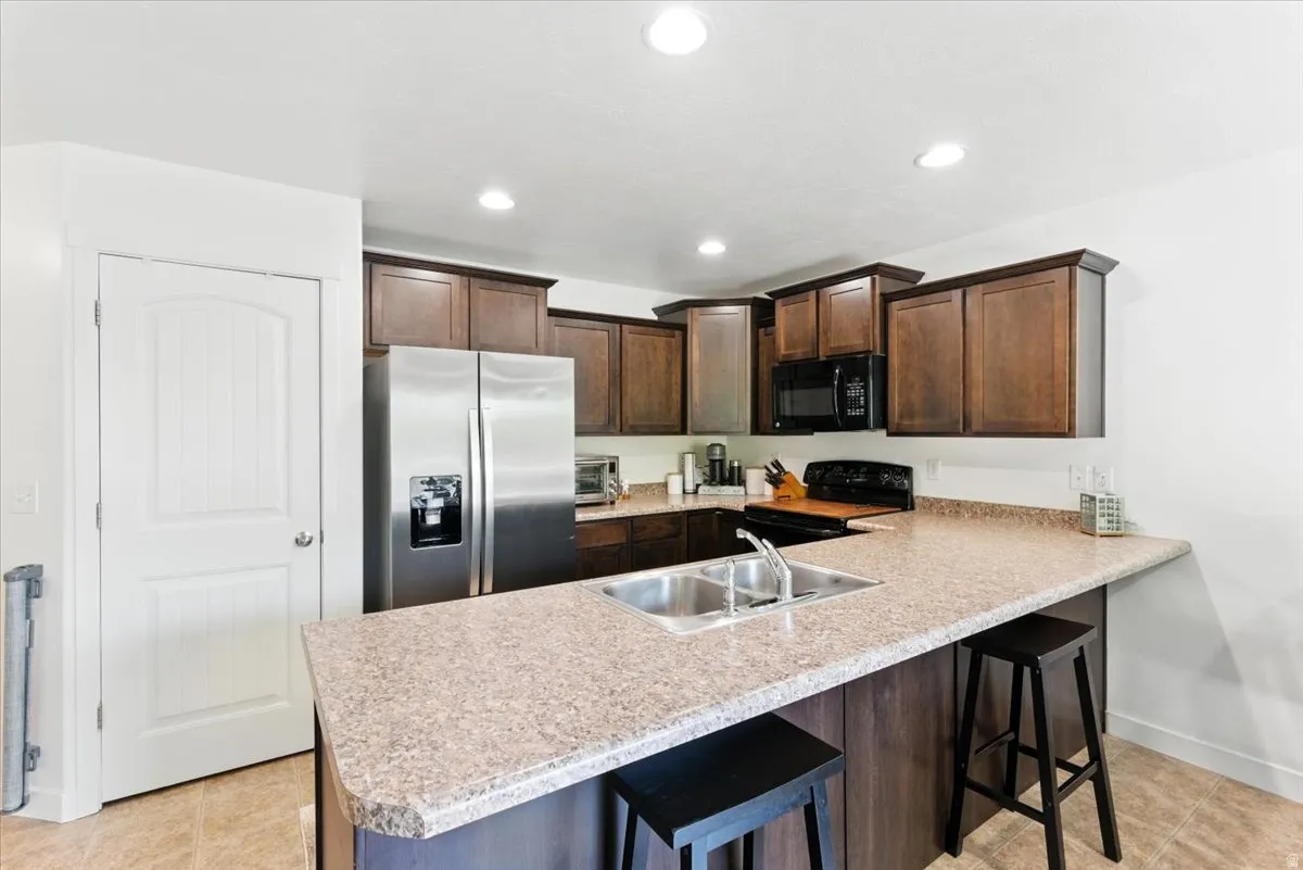 Kitchen featuring dark wood-finish cabinetry, light speckled countertops, a stainless-steel refrigerator, a built-in microwave, and recessed lighting