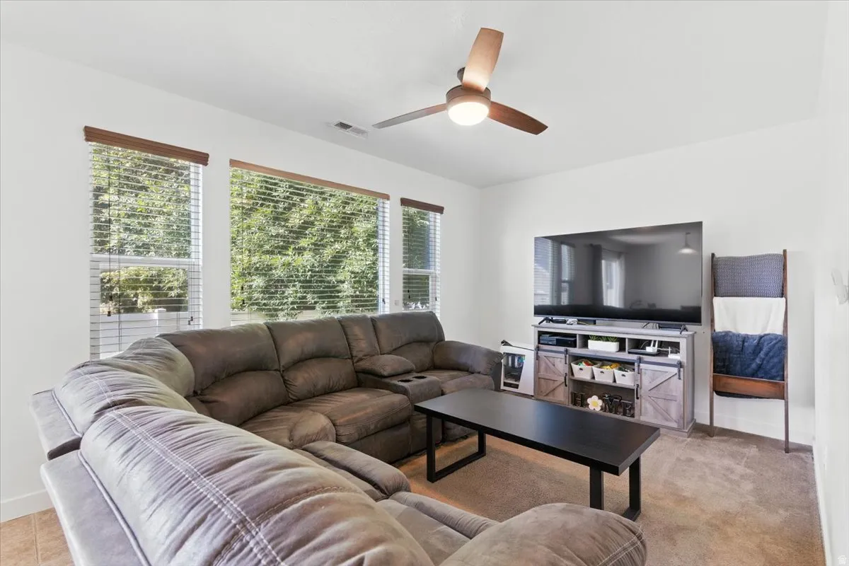 Bright living space with large windows, a ceiling fan with integrated lighting, and carpeted flooring