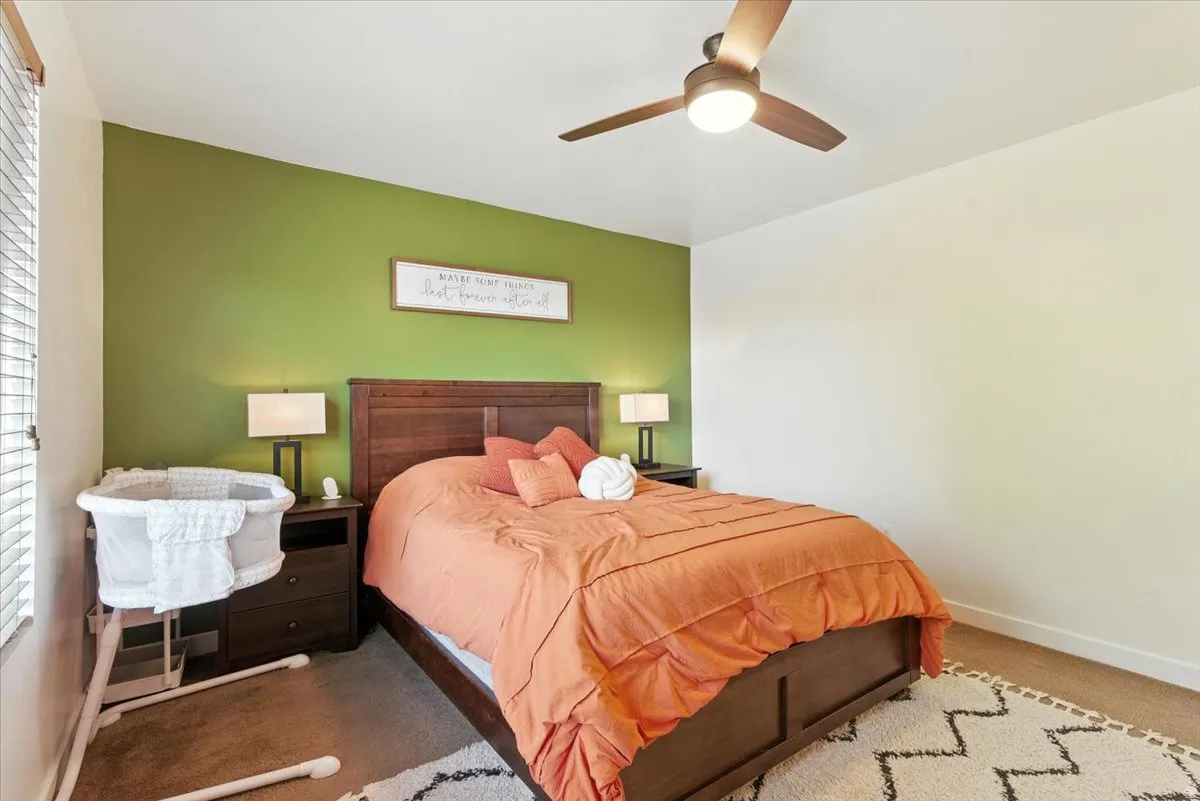 Angled accent wall, overhead ceiling fan with integrated lighting, window with horizontal blinds, and wood-finish flooring