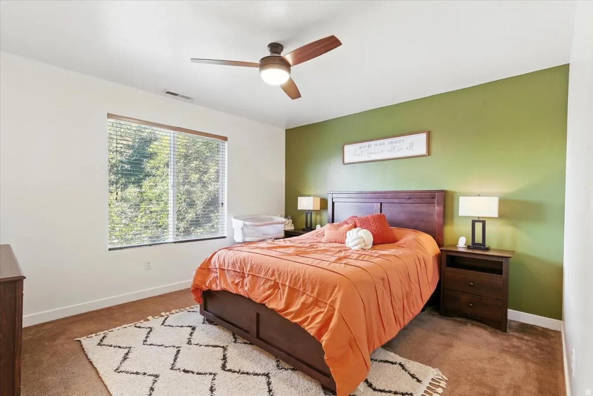 Carpeted room featuring a ceiling fan, a window with horizontal blinds, and a built-in headboard