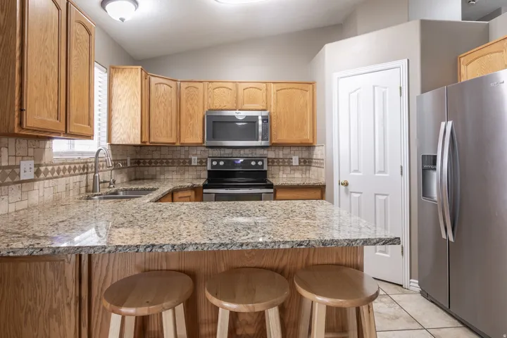 Kitchen featuring granite countertops, wood cabinetry, stainless steel appliances, and a tiled backsplash