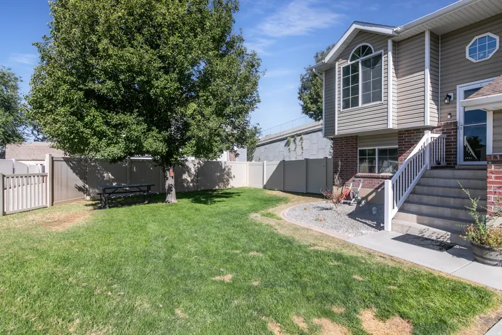 Manicured lawn with mature tree, fenced yard, concrete steps with white railing, and brick detailing on the facade