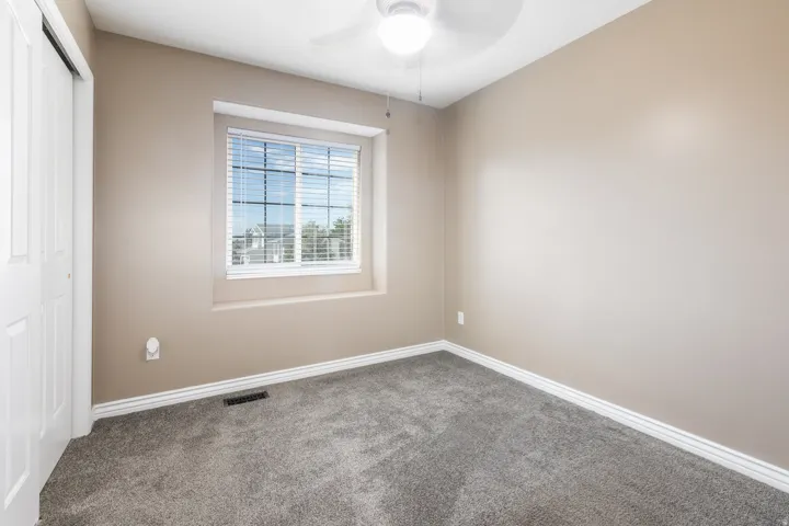Neutral tone paint, plush gray carpeting, overhead ceiling fan with lighting, white window blinds, and white bi-fold closet doors