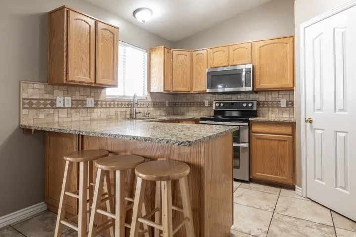 Kitchen featuring wood cabinetry, stainless steel appliances, a tile backsplash, light-toned countertops, and tile flooring