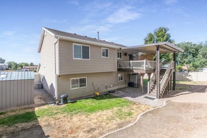 Two-story exterior with light-colored siding, covered deck, exterior staircase, and ground-level shed