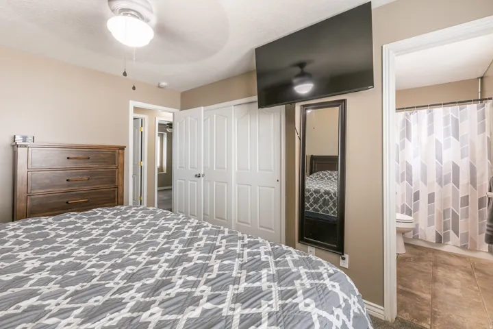 Neutral-toned walls, ceiling fan with integrated lighting, white bi-fold closet doors, tile flooring in the bathroom, and a full-length mirror