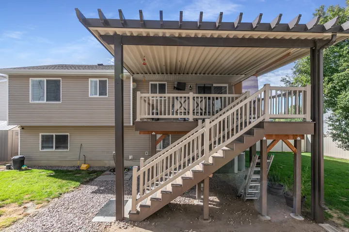 Expansive outdoor deck with white railing, covered patio featuring a slatted pergola, and exterior staircase