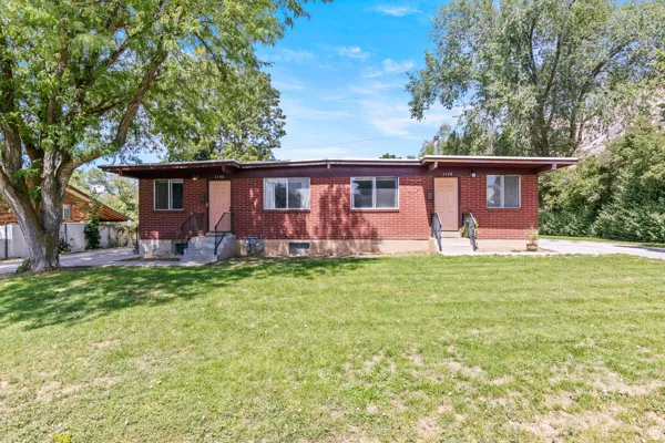 Brick exterior with dual entryways, concrete steps with metal handrails, and mature trees