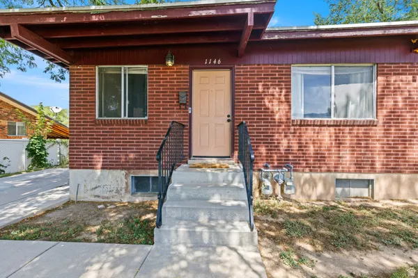 Brick exterior with a covered entry, concrete steps, and a black metal handrail