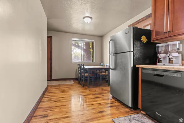 Wood-finish flooring, stainless steel refrigerator, built-in dishwasher, wood cabinetry, and a window