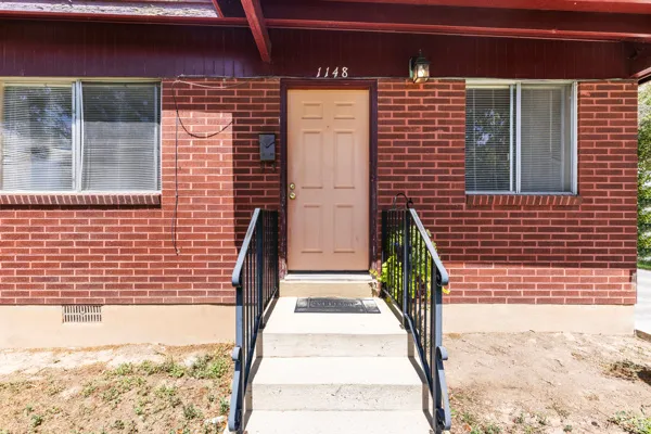 Welcoming front entrance featuring a brick facade, recessed door with sidelights, concrete walkway with black metal railings, and paired windows with white trim and privacy glass