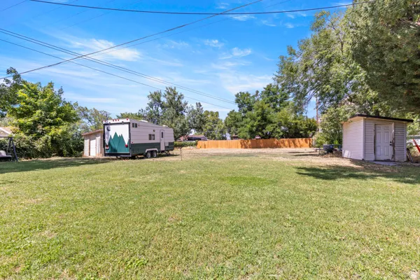 Expansive grassy area featuring a wooden privacy fence, mature trees, and an accessory storage shed