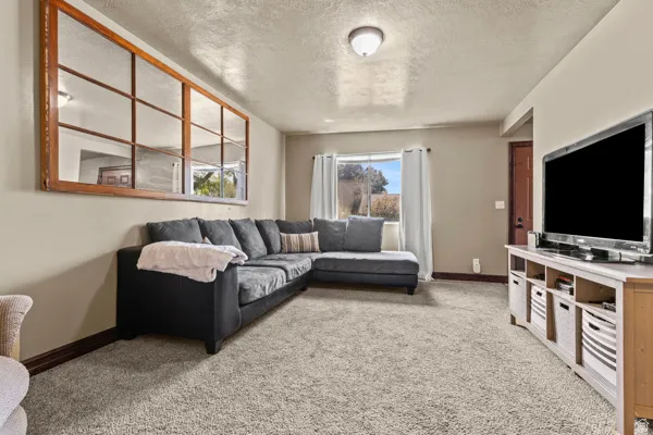 Neutral paint palette, textured ceiling, window with white curtains, wood-finish trim, and a prominent decorative mirror