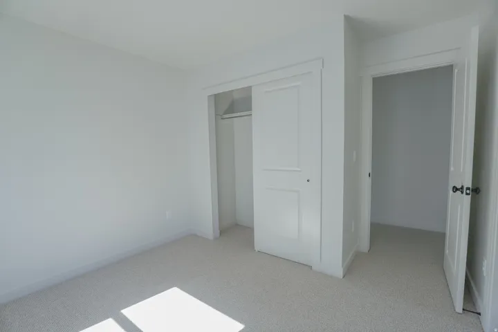 Neutral tone walls, light-colored carpet flooring, white trim, white panel doors, and a closet with a built-in rod