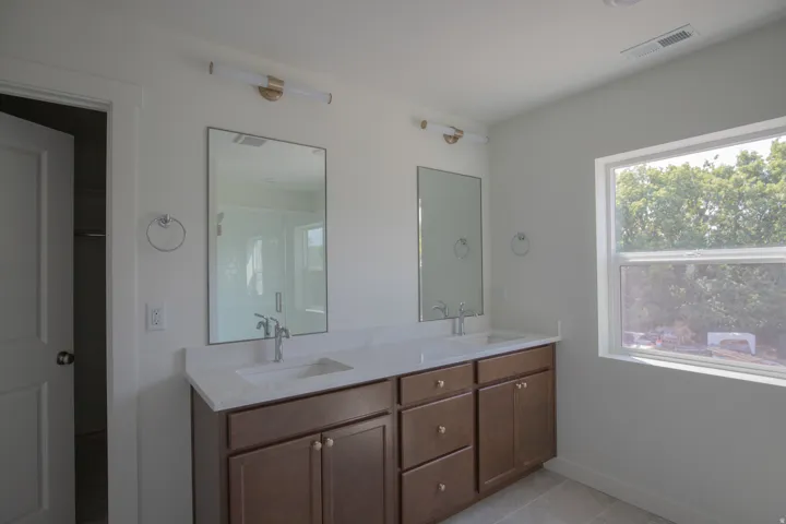 Dual vanity with integrated sinks and white countertops, individual wall-mounted mirrors, and sleek light fixtures