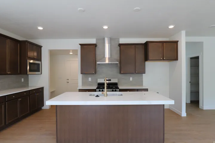 Expansive kitchen island with a white countertop, dark wood-finish cabinetry, stainless steel appliances, and wood-finish flooring