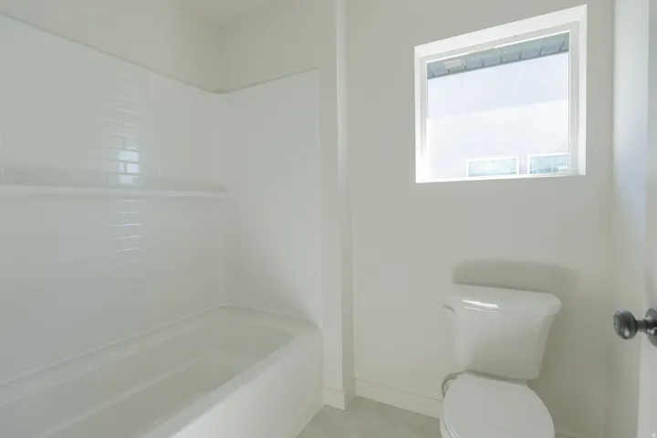 White subway tile shower surround with a built-in shelf, white porcelain bathtub, and an integrated toilet