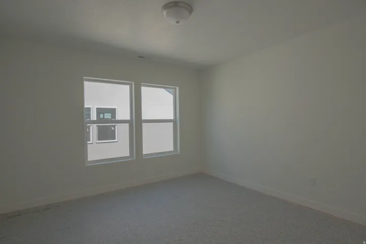 Light gray wall-to-wall carpeting, white painted walls, two rectangular windows with white frames, and a flush-mount ceiling light fixture