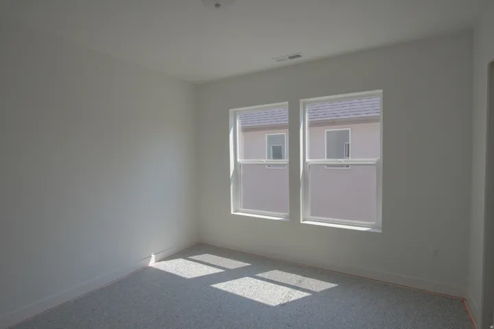 Light-filled room featuring two white-framed windows, neutral wall paint, and gray carpet flooring