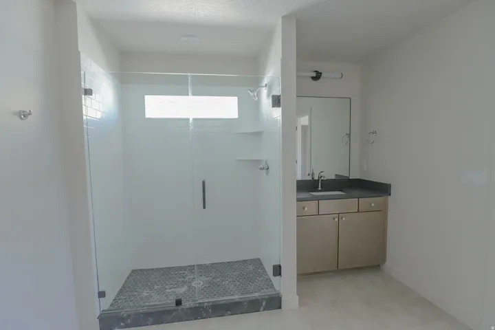 Glass-enclosed shower with white subway tile, a dark tile shower floor, and a transom window