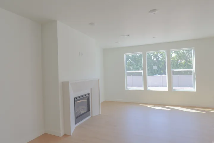 Integrated fireplace with a white mantel, wood-finish flooring, three large windows, and recessed ceiling lighting