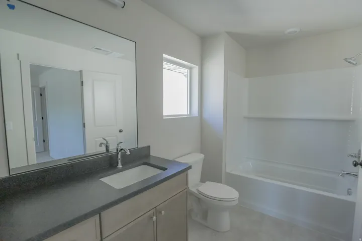 Neutral color palette bathroom featuring a built-in vanity with a dark countertop and undermount sink, a large frameless mirror, and a combined tub and shower unit with white subway tile