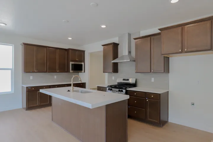 Expansive kitchen with shaker-style cabinetry, a central island featuring an undermount sink, stainless steel appliances, and wood-finish flooring