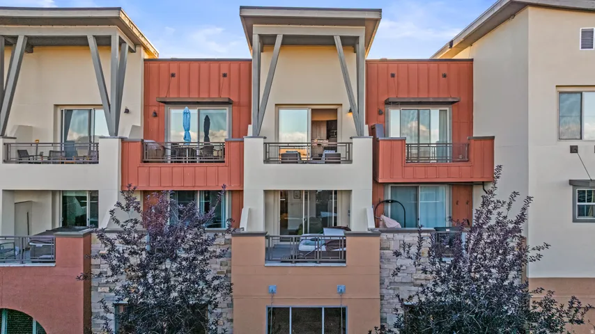 Multi-level residential exterior featuring private balconies with metal railings, sliding glass doors, and a stone facade detail
