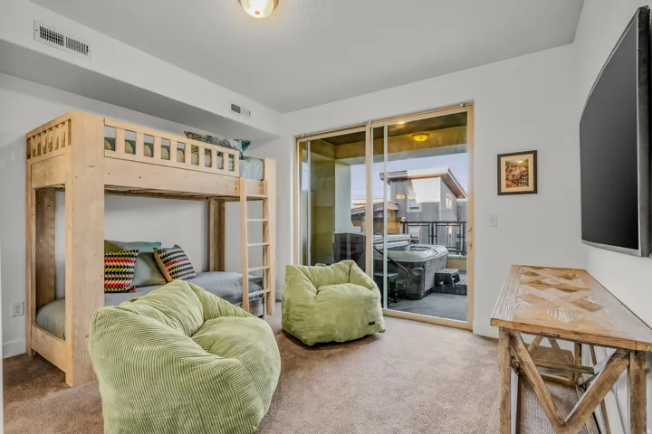 Built-in bunk beds, light beige carpeting, recessed ceiling light, sliding glass door access to an outdoor patio with a built-in hot tub, and a mounted television