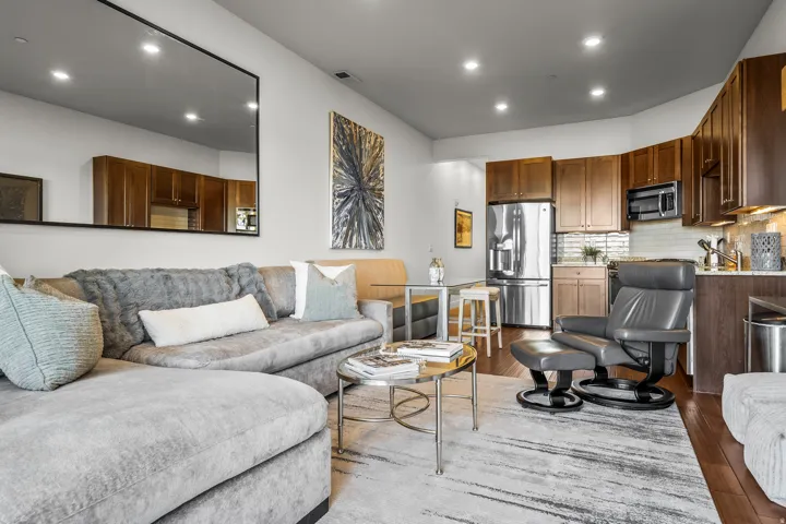 Recessed lighting illuminates the open-concept living area, featuring rich wood-finish flooring and a kitchen with stainless steel appliances, dark wood cabinetry, and a subway tile backsplash