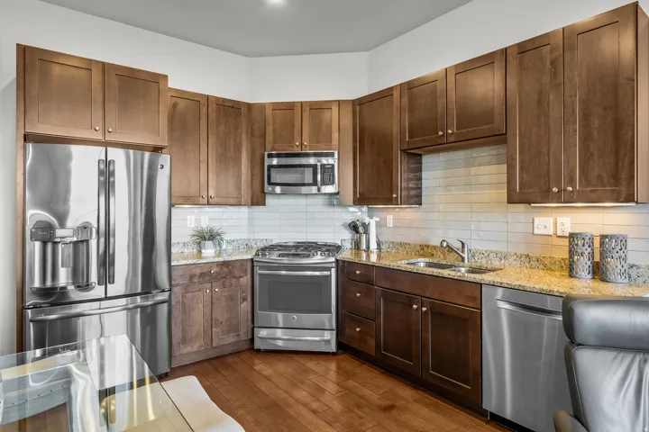 Kitchen featuring wood-finish flooring, stainless steel appliances, wood cabinetry, granite countertops, and a subway tile backsplash