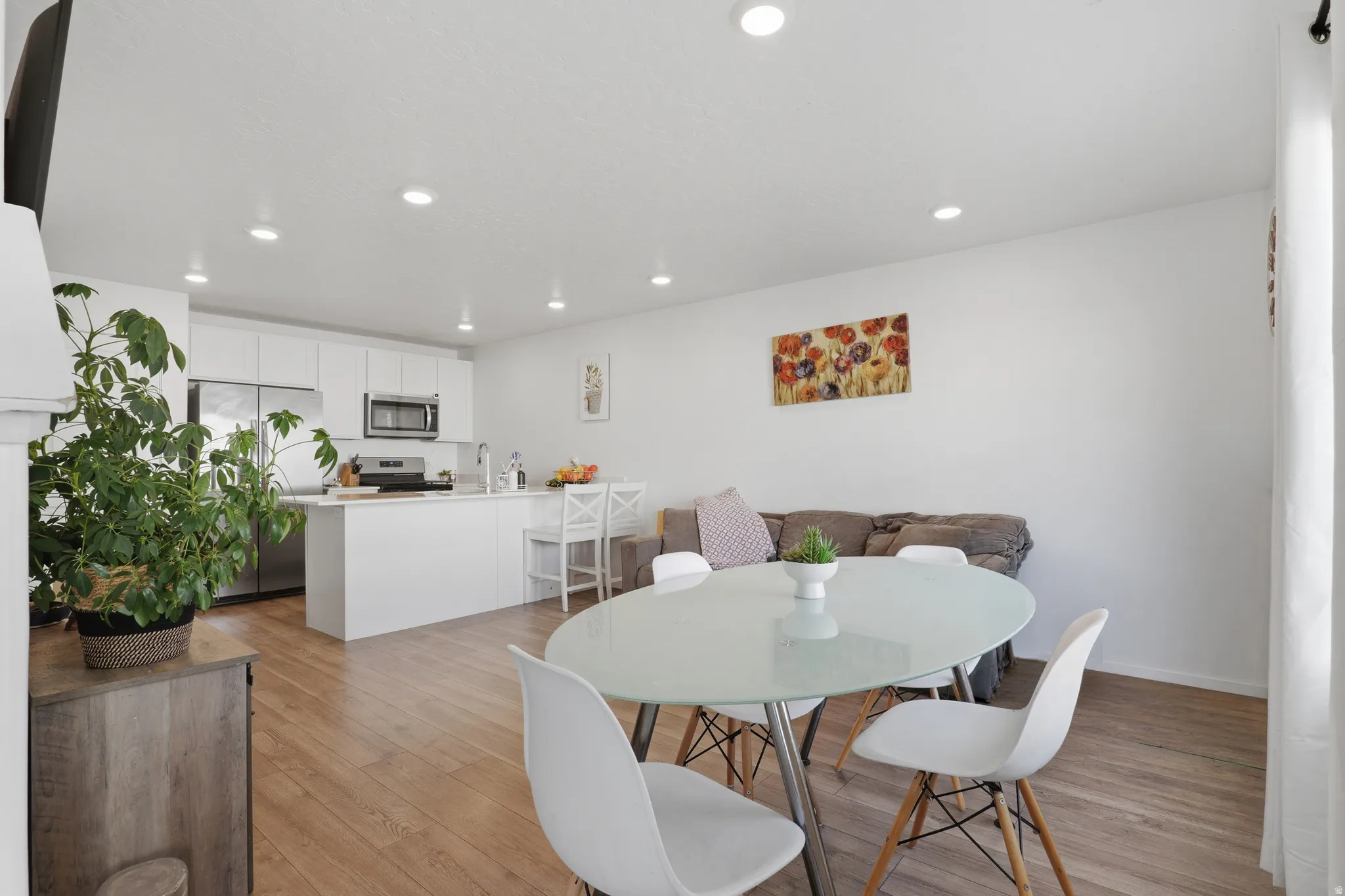 Wood-finish flooring throughout, recessed ceiling lighting, kitchen island with seating, stainless steel appliances, and white cabinetry