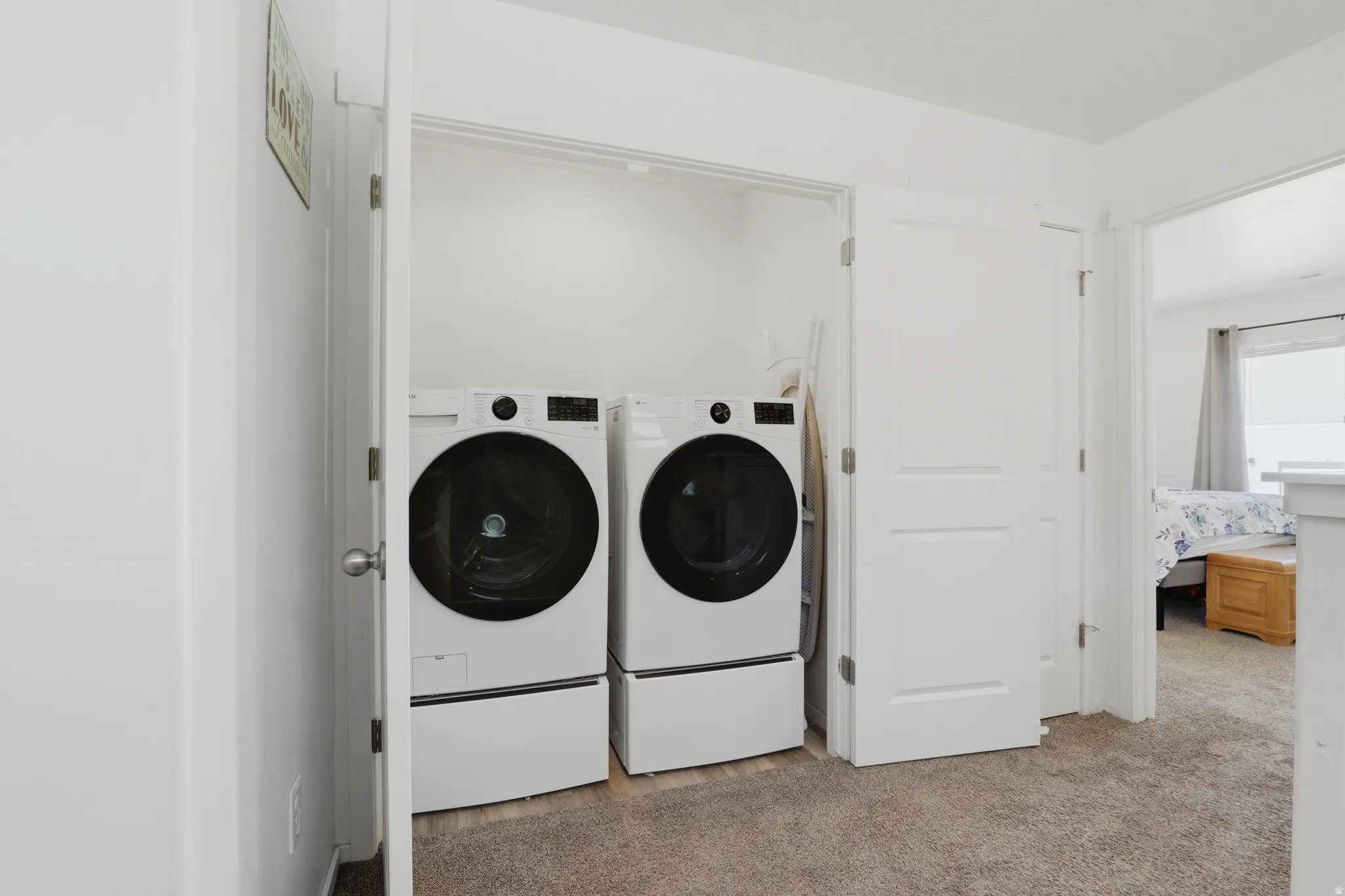 Laundry closet featuring double bifold doors, appliances on pedestals, and neutral carpeting