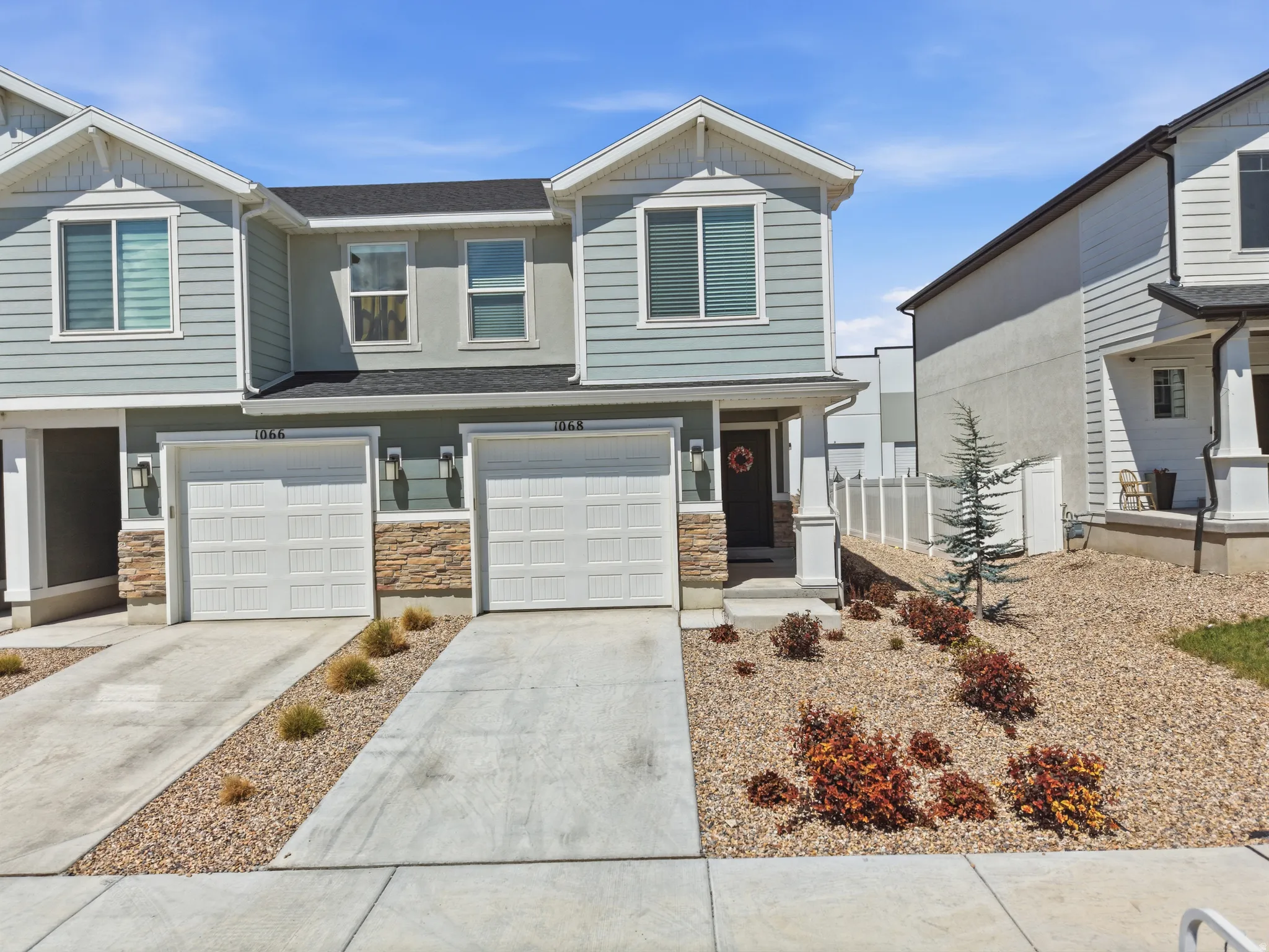 Contemporary townhouse with light blue siding, stone facade accents, two single-car garages, and a xeriscaped front yard