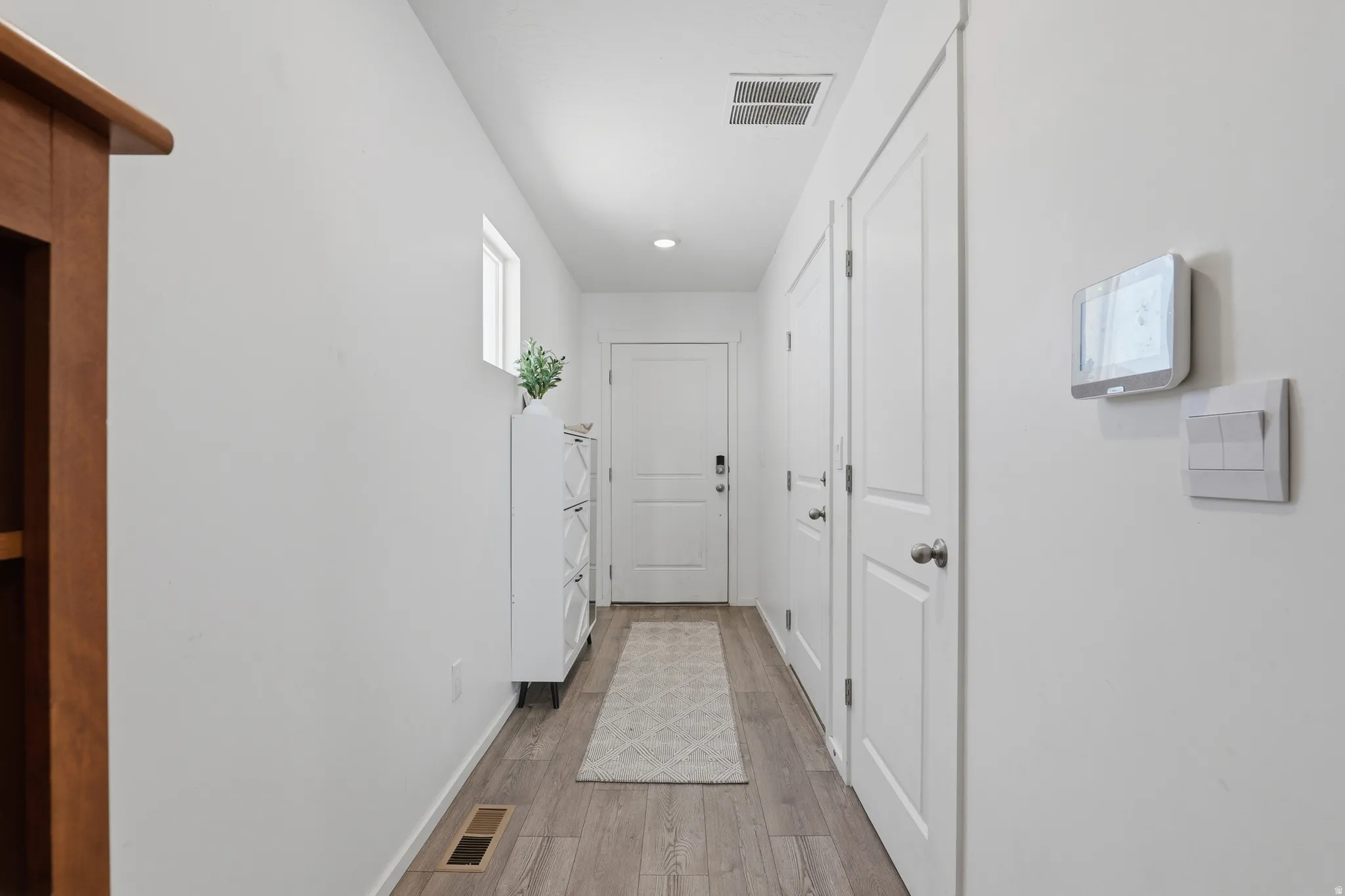 Hallway featuring wood-finish flooring, white paneled doors, and a built-in smart thermostat