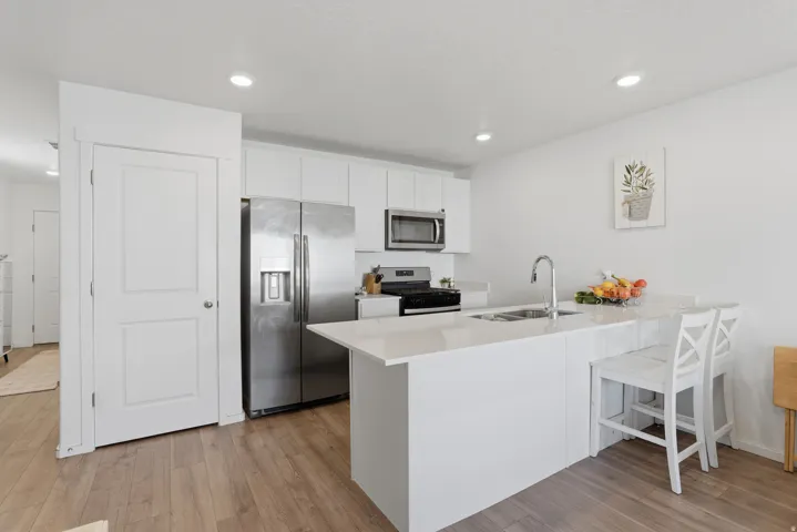 Kitchen featuring white cabinetry, stainless steel appliances, a center island with sink, light wood-finish flooring, and recessed lighting