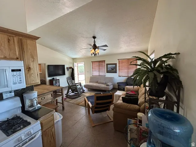 Vaulted ceilings with a ceiling fan, wood-finish cabinetry, tile flooring, and integrated kitchen appliances
