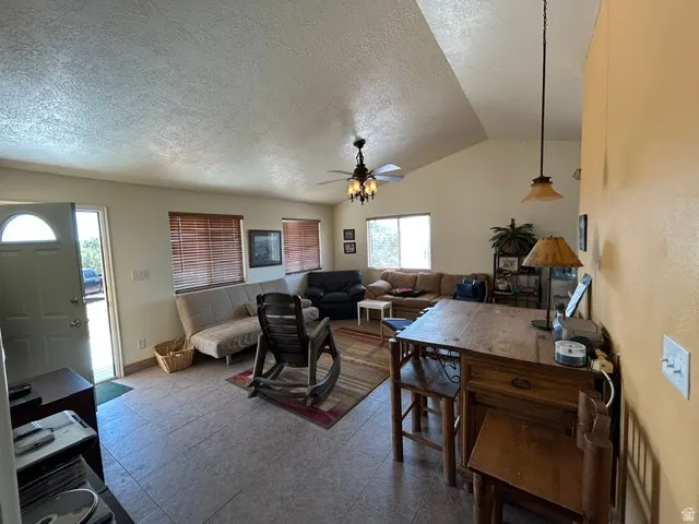 Vaulted ceiling, tiled flooring, ceiling fan with integrated lighting, multiple windows with blinds, and a suspended dining light fixture
