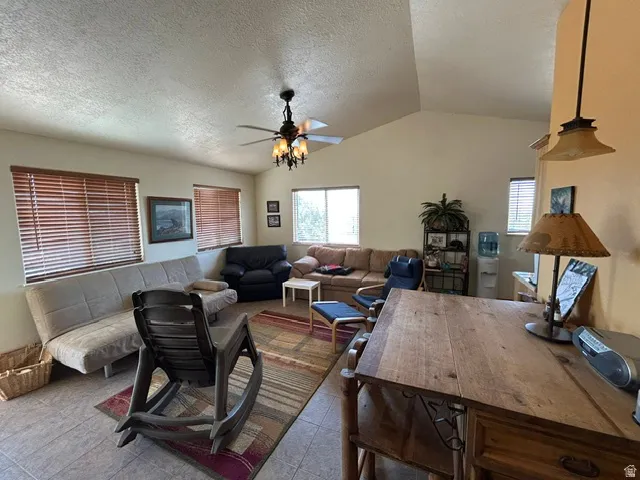 Vaulted ceiling with a ceiling fan light fixture, multiple windows with blinds, and tile flooring
