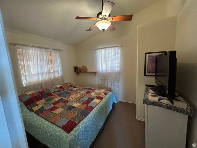 Vaulted ceiling with a ceiling fan, two windows with blinds, wall-mounted shelving, and neutral wall paint