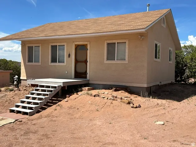 Stucco exterior with multiple windows, wooden entry door, and an elevated front deck with stairs